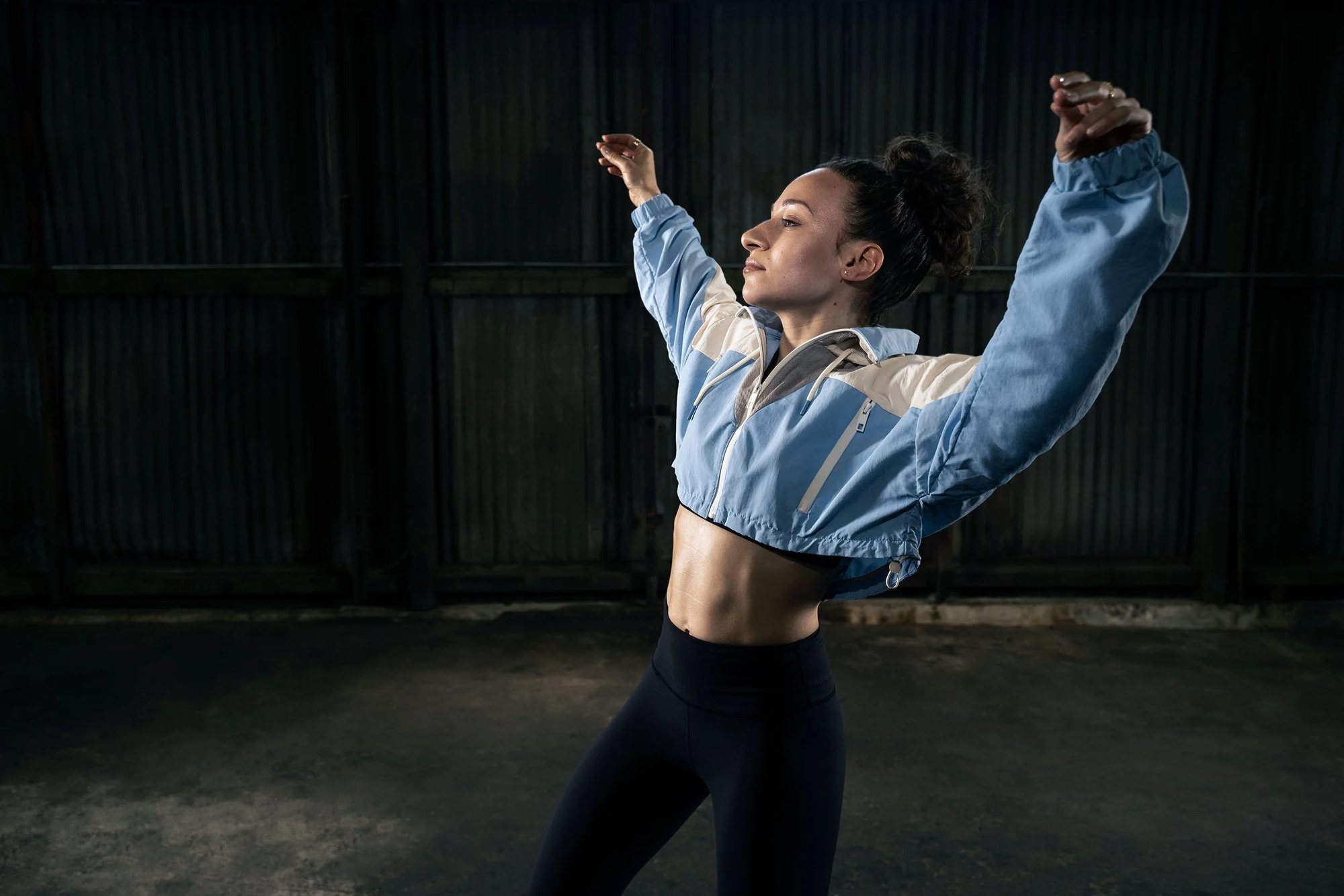 Galit Friedlander in a dark warehouse, arms thrown wide, in a cropped denim jacket